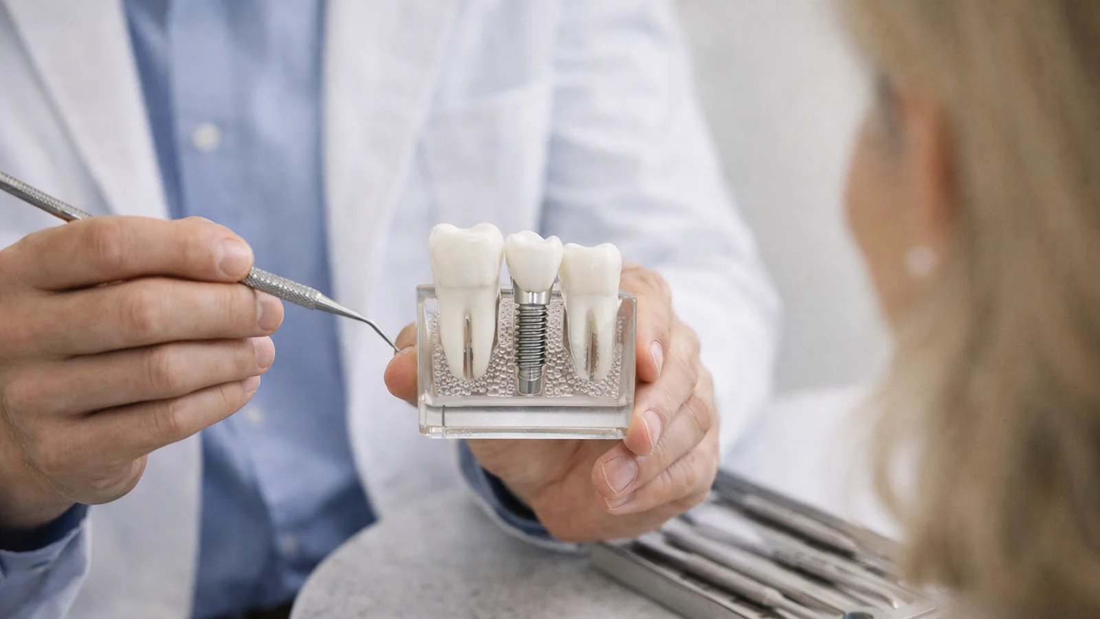 Dental implant model being explained chairside with instruments nearby for a patient consultation.
