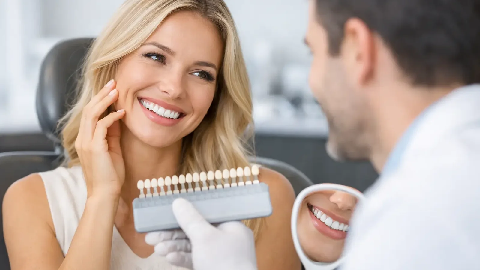 Veneers consultation with a dentist showing a shade guide while the patient reviews her smile in a mirror.